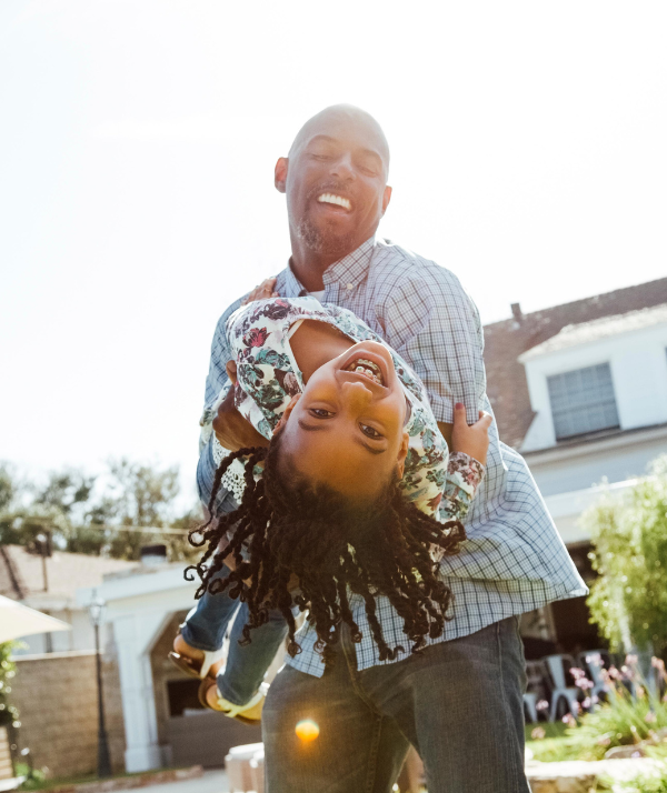 Father playing with his smiling young child in front of their house on a sunny day